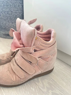 Rosa sneakers med klack och kardborre - Unika rosa sneakers med klack och breda kardborreband. Skorna har en cool, oversized plös och är gjorda i mjukt mockaliknande material. Isabel marant liknande skor men vet inte om de är äkta. Köpt på Vinted för 1000kr. Vid snabb affär kan pris diskuteras. 