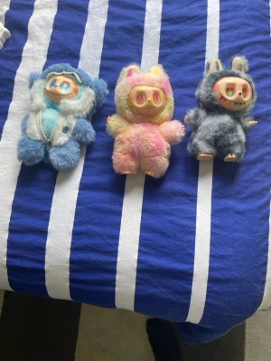 Tre färgglada dockor i djurdräkter - Säljer tre gulliga dockor med stora ögon, klädda i mjuka djurdräkter. En har blå och vit björndräkt, en har rosa och gul dräkt med kattöron, och en har grå kanindräkt med små tänder. Perfekta som samlarprylar eller dekoration.