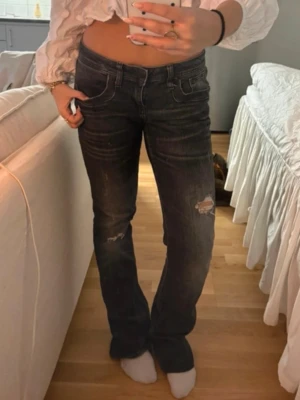 Mörkblå bootcut jeans med slitningar från ltb  - Säljer ett par mörkgråa bootcut jeans med slitna detaljer på låren och knäna. Jeansen har klassisk femficksmodell, låg midja och kontrastsömmar. Materialet är denim i bomull med lite stretch för skön passform.