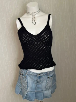 Svart stickad linnetopp - Svart stickad linnetopp med smala axelband och v-ringning både fram och bak. Toppen har ett genomgående rutmönster och är lätt transparent, perfekt för lager-på-lager-stil. Snygg och enkel att matcha med jeans eller kjol.