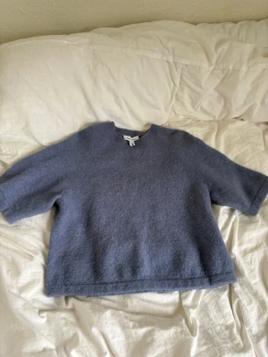 Blå stickad tröja med korta ärmar - En enkel och stilren blå stickad tröja med korta ärmar och rund hals. Tröjan har en lite oversiced passform men på ett snyggt sätt och är gjord i ett mjukt material. Nästan oanvänd och säljer för att färgen ej passar på mig. 