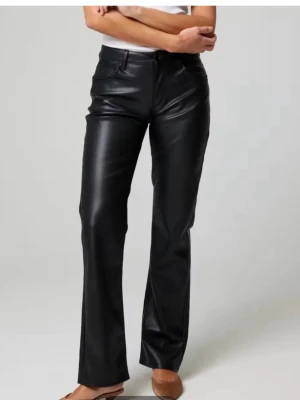 Svarta raka byxor i skinnimitation - Snygga svarta byxor med rak passform i skinnimitation. De är helt nya, oanvända med prislapp, säljer då de ej kommer till användning! Byxorna har klassiska fickor fram och bak, samt knapp och dragkedja i midjan. Dessa går även  inte att köpa i affär längre. 