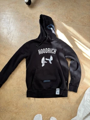 Svart hoodie från Hoodrich - Svart hoodie från Hoodrich med stor vit logga och två duvor på bröstet. Säljer då den inte används. Går ner i pris vid snabbt köp.