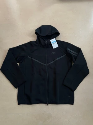 Nike tech fleece zip hoodie svart storlek medium - Nike Tech Fleece hoodie i nyskick. En av de mest populära Nike-plaggen just nu.  Oanvänd Perfekt året runt Väldigt hög efterfrågan  Skickas direkt 🚚 Bundle-rabatt finns.