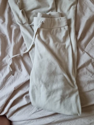 Vita mjukisbyxor med dragsko - Säljer ett par vita  mjukisbyxor med resår i midjan och vit dragsko. Byxorna har utsvängda ben och är gjorda i ett mjukt, skönt material som känns riktigt chill. Perfekta för att slappa hemma eller hänga med vänner.