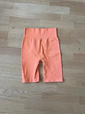 Ribbstickade orangea leggings Gina Tricot - Snygga ribbstickade leggings i en fräsch orange färg från Gina Tricot. Modellen har hög midja och kortare benlängd, perfekt för en trendig och bekväm look. Tillverkade i stretchigt material som sitter skönt hela dagen. Aldrig använda!