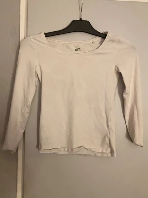 Vit långärmad topp från 157 - En enkel och stilren vit långärmad topp från 157 med rund halsringning. Perfekt att matcha med jeans eller kjol. Materialet känns mjukt och bekvämt, troligen bomull. Passformen är normal och toppen är utan mönster eller detaljer.