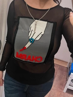 Vår Svart mesh topp med CHARM-tryck - Snygg svart mesh topp med lång ärm och ett stort grafiskt tryck framtill med texten..