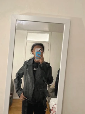 Svart biker skinnjacka med bälte - Cool svart skinnjacka i klassisk bikerstil med sned dragkedja, axelklaffar och bälte i midjan. Jackan har flera fickor med dragkedja och detaljer i silver. Perfekt för en edgy look. Har inte använts och är helt ny😍😍😊