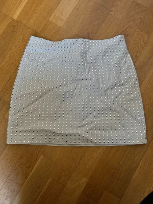 Beige kortkjol med nitar från H&M - Snygg beige kortkjol från H&M dekorerad med små silverfärgade nitar över hela kjolen. Kjolen har en rak passform och dragkedja i sidan. Perfekt för dig som vill sticka ut lite extra. Tar emot prisförslag 