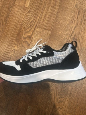 B25 - Snygga sneakers  i svart och vitt med tydlig logga på sidan. Skorna har en chunky vit sula, svarta mockadetaljer och meshpartier för extra ventilation. Klassisk snörning och modern design som sticker ut.