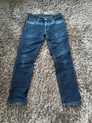 Levi's blå raka jeans - Klassiska blå jeans från Levi's med rak passform och fem fickor. Jeansen har tydliga kontrastsömmar och en ikonisk läderpatch bak i midjan. Tillverkade i slitstark denim med snygg tvätt och subtila slitningar. Perfekta för en avslappnad och tidlös stil. W30 L32