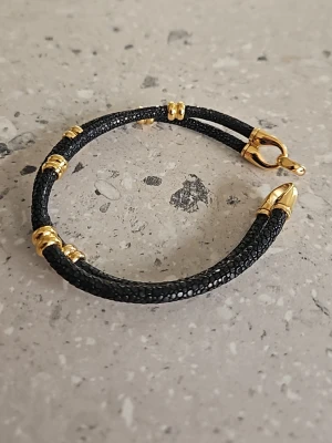 Svart armband med gulddetaljer - Snyggt svart armband med struktur och flera guldfärgade detaljer samt ett elegant guldfärgat lås. Armbandet har en modern och stilren design som passar perfekt till en trendig look. 