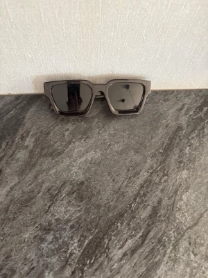 Svarta solglasögon från Jack & Jones - Snygga svarta solglasögon från Jack & Jones med rektangulära bågar och mörka glas. Ramen är i plast och har en modern, kantig design som ger en cool vibe. Perfekta för att lyfta din stil under soliga dagar.