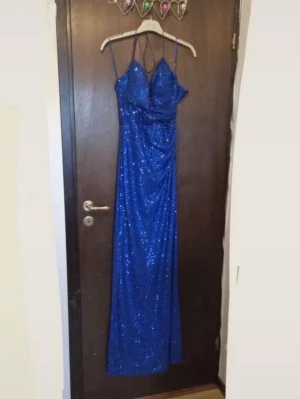 Blå balkläning - Snygg blå balklänning med paljetter och smala axelband. Klänningen har en figurnära passform och djup v-ringning framtill. Perfekt för bal eller festliga tillfällen där du vill sticka ut. Köpt för 2000kr och använd endast en gång.