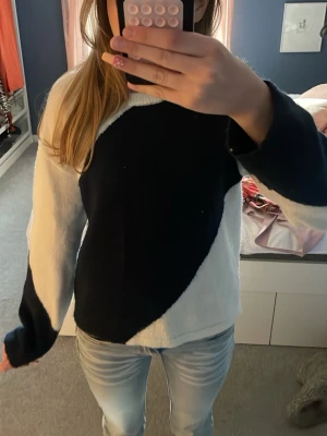 Svartvit stickad tröja med mönster - Säljer en cool stickad tröja i svart och vitt med ett stort, böljande mönster över hela tröjan. Tröjan har rund hals och långa ärmar, perfekt för dig som gillar att sticka ut lite. Passar till jeans och är riktigt skön att ha på sig.