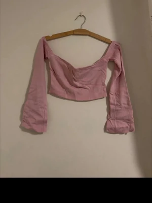 Ljusrosa croppad topp med offshoulder - Trendig ljusrosa croppad topp med offshoulder och långa, utsvängda ärmar.