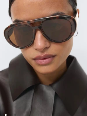 Bold Aviator sunglasses - Snygga solglasögon från Gina Tricot med bruna pilotbågar i sköldpaddsmönster och mörka linser. Ramen är i syntetmaterial och har en cool, oversized look som verkligen sticker ut. Perfekta för att ge din outfit en trendig touch.