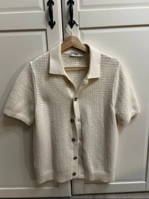 Vit kortärmad stickad kofta från Mango - pris kan diskuteras  - Kortärmad stickad kofta i vit färg med genomgående knappar framtill och klassisk krage. Koftan har ett luftigt hålmönster och ribbade kanter vid ärmslut och nederkant. Perfekt för lager på lager och en clean look. Använd en gång. 