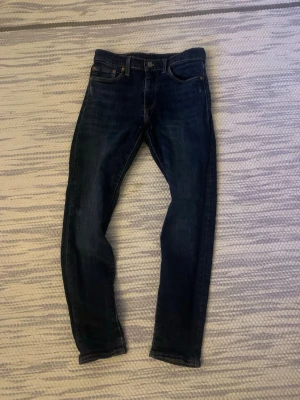 Levis 512 slim fit - Snygga mörkblå slim fit jeans från Levis med klassisk femficksdesign och orangea sömmar. Jeansen har en låg midja och är tillverkade i ett stretchigt denimtyg som ger en skön passform. Perfekta för dig som gillar en stilren och enkel look.