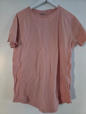 Ljusrosa t-shirt från Jack & Jones - En enkel och stilren ljusrosa t-shirt från Jack & Jones Essentials. Tillverkad i mjuk ekologisk bomull med klassisk rund hals och korta ärmar. Perfekt basplagg för en avslappnad look.
