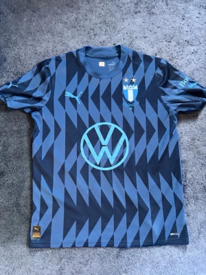 Autograf malmö tröja  - Säljer en signerad Malmö FF-tröja från 2024. Tröjan är i fint skick och har flera autografer från spelare i laget, samtliga signerade under 2024. Den har en stilren mörk design med ljusblå detaljer och klubbmärket på bröstet. Tröjan är i barnstorlek 158/164. Priset kan diskuteras, signaturerna hitter ni här ner👇  Signerad av: Isaac Kiese Thelin, Taha Ali, Anders Christiansen, Pontus Jansson, Sebastian Nanasi, Oliver Berg, Sergio Peña, Erik Botheim, Johan Dahlin, Hugo Bolin och Ricardo Friedrich.