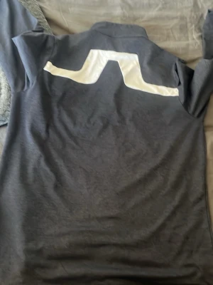 Blå golftröja från J.Lindeberg - Riktigt bra skick använd en gång köpte fel storlek nypris 999, Snygg mörkgrå golf tröja  från J.Lindeberg med stor vit logga på ryggen