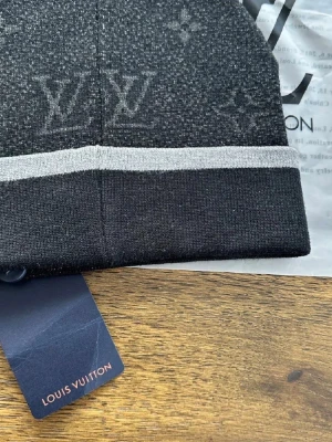 Svart mössa från m - Snygg svart mössa från m med grått monogrammönster och en ljusgrå rand. Märkets logga är broderad framtill och materialet känns mjukt och stretchigt, perfekt för kalla dagar. En stilren accessoar som lyfter din outfit.  (taggsen är borta)