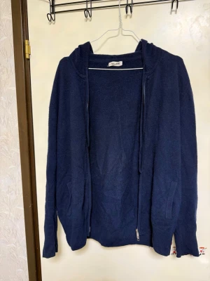 Mörkblå hoodie i kashmir från Soft Goat - Mysig mörkblå hoodie från Soft Goat i mjuk kashmir. Tröjan har dragkedja framtill, huva och två fickor på sidorna. Perfekt för dig som gillar stilrena och bekväma plagg med en lyxig känsla.