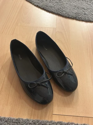 Mörkblåa ballerinaskor - Stilrena mörkblå ballerinaskor från Nelly med blank finish och en liten rosett framtill. Använda endast en gång. Snörerna har gått upp lite men det går enkelt att knyta om💙