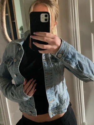 Ljusblå cropped jeansjacka - Trendig ljusblå jeansjacka med kort, croppad passform och klassiska silverknappar. Perfekt att slänga över en t-shirt för en avslappnad look. Hör av dig vid behov av fler bilder 