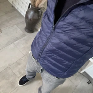 Navy Väst  - Snygg mörkblå dunväst med quiltad design och hög krage. Västen har hel dragkedja framtill och är lätt vadderad för extra värme. 