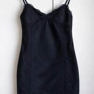 Svart kort klänning med spetsdetaljer - LBD - Stilren svart kort klänning med smala axelband och spetsdetaljer upptill. Klänningen har en figurnära passform och dragkedja i sidan för enkel påklädning. Perfekt för dig som gillar en klassisk och elegant look. M men passa S storlek 