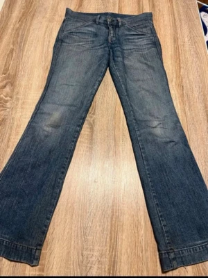 Blå bootcut jeans med fickdetaljer - Ett par klassiska blå bootcut jeans i denim med snygga fickdetaljer och kontrastsömmar. Jeansen har vida ben och metallknappar på fickorna. Perfekta för en avslappnad och trendig look.