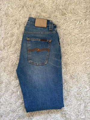 Blå jeans från Nudie Jeans - Säljer ett par blåa jeans ifrån nudie. Dem är i mycket bra skick och är endast prövade.       Modell: Grim Tim                                                       Storlek: W30 L32