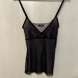 Svart linne från Sisters - Snyggn svart linne från Sisters med smala axelband och v-ringning. Perfekt för lager-på-lager eller som statement-plagg. Enkel och stilren design som passar till många olika outfits.