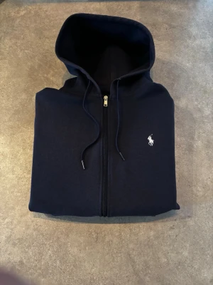 Mörkblå hoodie | Polo Ralph Lauren - Strl M  - Snygg och tidlös zip hoodie från Polo Ralph Lauren i klassisk mörkblå färg. 🤩Vit broderad logga på bröstet.  ✅Storlek M, mycket fint skick. ✅Perfekt basic som funkar året runt
