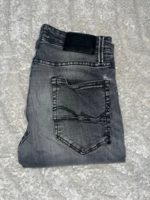 Jack & Jones jeans  - Jeans från Jack & Jones i grå tvätt med fade, modell Glenn som har en slim fit passform. Midja 33cm, längd 110cm. Obs jeansen har defekter. Baktill i det stora inringade området är tyget förtunnat. De två mindre omringade är det hål som slutessamman med trådar över. Obs storlekslapp saknas men jag skulle bedöma till w27 L34 men utgå efter mått. JAG SKICKAR EJ FLER BILDER NÄR JAG BÄR JEANSEN! för bättre inblick i passformen rekommenderar jag att googla på modellnamnet. Tar ej emot returer:)1,60