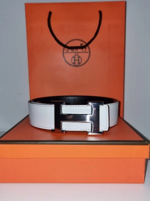 H bälte - Snyggt vitt skärp från H med ikoniskt stort H spänne i silverfärgad metall. Bältet är gjort i exklusivt skinn och har stilrena sömmar längs kanterna. Perfekt accessoar för att lyfta vilken outfit som helst.