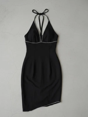 Svart halterneckklänning med pärldetaljer - Svart kort halterneckklänning med smickrande passform och dekorativa pärlor längs urringning och nederkant. Klänningen har knyt i nacken och en djup v-ringning som ger en elegant look. Perfekt för dig som vill sticka ut med stilrena detaljer.  Se bild två för defekt går att laga. Annars ny skick 