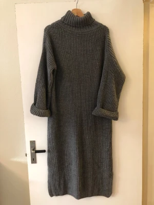 Grå stickad poloklänning - Mysig STOR härlig grå stickad klänning med polokrage och långa ärmar. Klänningen har en rak passform och ribbstickad struktur, perfekt för lager på lager och en avslappnad stil. Ärmarna är uppvikta för en cool touch.