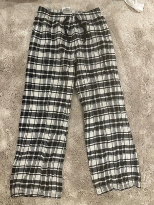 Rutiga pyjamasbyxor i svart och vitt - Mysiga pyjamasbyxor med svartvitt rutmönster och dragsko i midjan. Byxorna har raka ben och elastisk midja för extra komfort. Perfekta för chillkvällar hemma. Tillverkade i mjukt tyg som känns skönt mot huden.