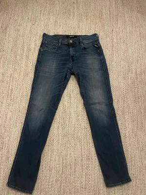 Replay Hyperflex blå jeans - Säljer ett par snygga blå jeans från Replay, modell Hyperflex. Jeansen har en klassisk femficksdesign, smal passform och coola slitningar framtill. Tillverkade i stretchigt denim för extra komfort. Perfekta till en avslappnad streetwear-look.