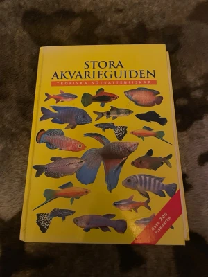 Stora Akvarieguiden bok - Stora Akvarieguiden: Tropiska sötvattensfiskar är en färgglad bok med gul hård pärm och illustrationer av olika fiskar på omslaget. Perfekt för dig som vill lära dig mer om över 200 fiskarter till akvariet.
