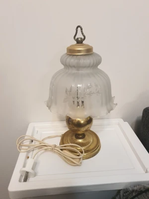 Bordslampa i glas och mässing - Säljer en vintage bordslampa med frostat glas och dekorativt blommönster på skärmen. Lampan har guldfärgad fot i mässing och vit sladd med stickkontakt. Klassisk och elegant design som passar perfekt som inredningsdetalj.