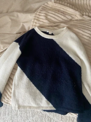 Stickad tröja med svartvit diagonal - Snygg stickad tröja med bred diagonal svart rand över vit botten. Tröjan har rund halsringning och långa ärmar. Perfekt för dig som gillar grafiska mönster och vill ha en unik look. Mjuk och skön att bära.