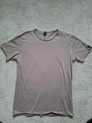 Beige t-shirt från Replay - En enkel och stilren beige t-shirt från Replay med rund halsringning och korta ärmar. Tillverkad i mjuk bomull för en skön känsla. Perfekt basplagg till garderoben och lätt att matcha med olika stilar.