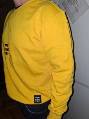Gul sweatshirt från MSGM - Gul sweatshirt från MSGM med stor svart text på ryggen och ärmarna. Tröjan har rund halsringning, ribbade muddar och en relaxed passform. Tillverkad i mjukt material som känns skönt mot huden. Perfekt för dig som gillar streetwear och vill ha ett statement-plagg.