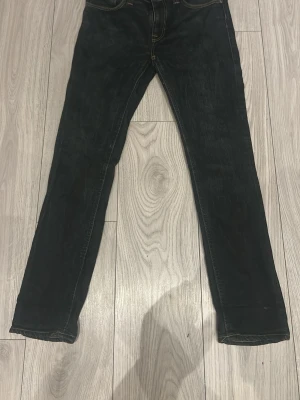 Svarta jeans från Nudie Jeans - Säljer ett par svarta jeans från Nudie Jeans med klassisk femficksdesign och raka ben. Jeansen har kontrastsömmar och Nudie Jeans ikoniska broderi på bakfickorna. Tillverkade i slitstark denim, perfekta för en avslappnad och stilren look. Dem kostar 1600kr nya. Mitt pris 349kr. Det är lätt strech på dem 