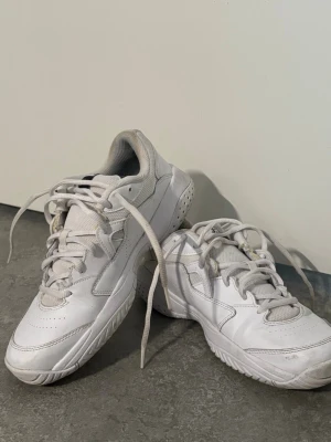 Vita Nike sneakers med svart swoosh - Säljer ett par klassiska vita Nike sneakers med svart swoosh på sidan. Skorna har lågt skaft, vita snören och detaljer i vitt läder samt mesh vid plösen. Perfekta för dig som gillar en clean och sportig look.